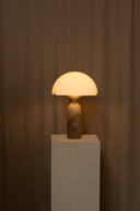 Table lamp with a warm glow on a white pedestal against a brown curtain background