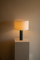 Table lamp with a beige shade on a gray pedestal against a brown background