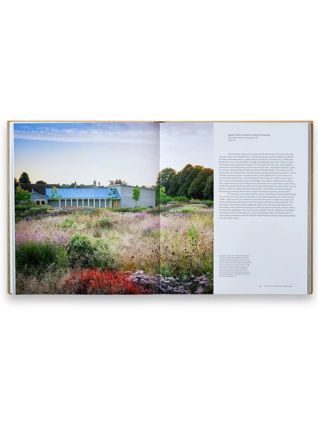 Book Piet Oudolf at Work, an open hardcover book displaying a vibrant photograph of Oudolf Field at Hauser & Wirth Somerset, featuring a modern building with a blue roof, surrounded by a diverse, naturalistic garden with wildflowers in shades of red, purple, and green. This essential gardening book offers inspiring landscape design ideas and detailed insights for garden enthusiasts and professional landscapers.