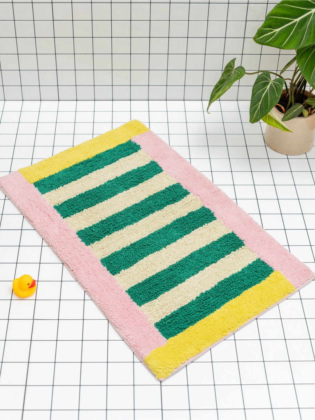 TARTA GELATINA Piña Colada Bath Mat, a vibrant striped bath mat featuring bold green and cream horizontal stripes, framed by a playful pink border with sunshine yellow accents at the top and bottom. Crafted from plush, tufted cotton for a soft, absorbent feel, this colorful rectangular bath mat is perfect for adding retro charm and a pop of color to any modern bathroom or kids' washroom.
