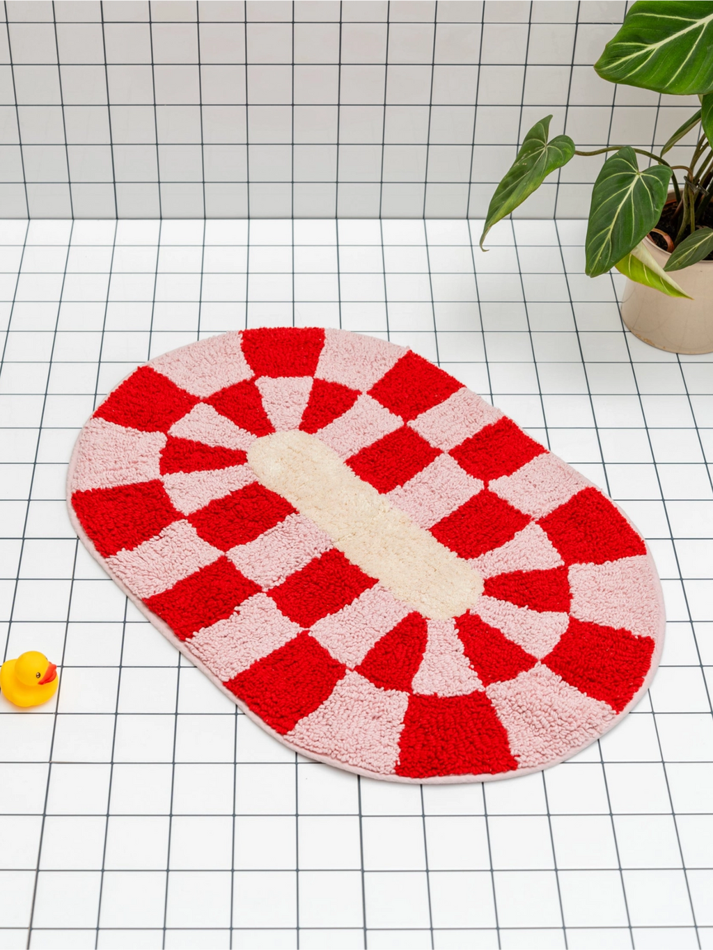 TARTA GELATINA Rita Bath Mat, a playful oval tufted cotton bath mat featuring a vibrant red and blush pink checkerboard pattern radiating around a cream central oval. This soft and absorbent geometric bath mat offers a whimsical retro design with a plush texture. Perfect for adding a colorful accent to modern bathrooms, kids' rooms, or playful powder rooms.