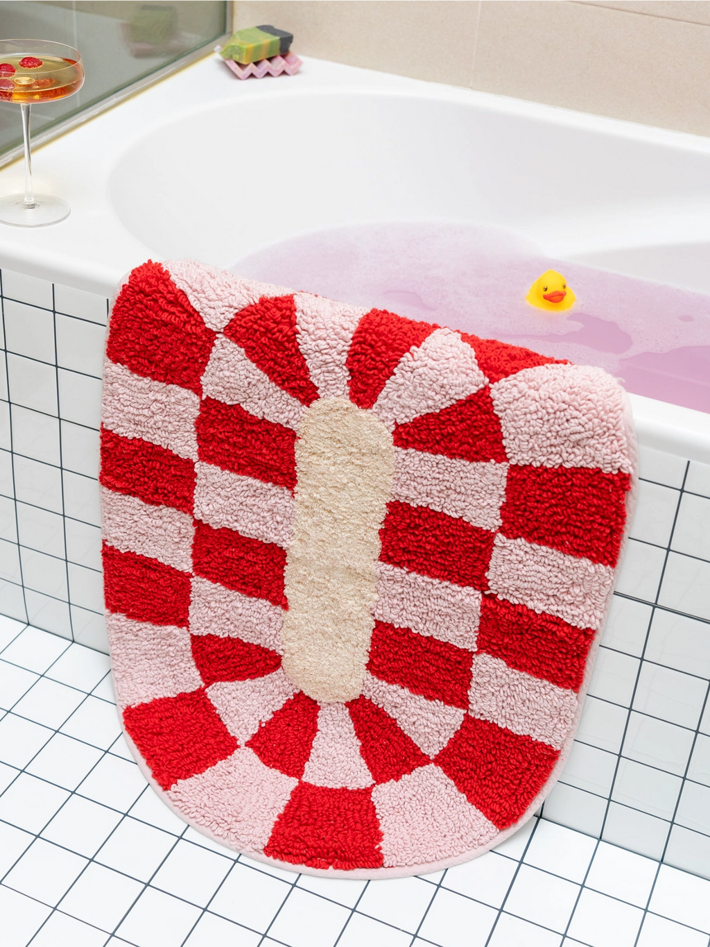 TARTA GELATINA Rita Bath Mat, a vibrant half-round tufted cotton bath mat featuring a playful red and pale pink checkerboard sunburst pattern surrounding a natural cream oval center. This shaggy and plush bath mat adds a cheerful, retro touch to any bathroom decor, perfect for maximalist or colorful bathroom styles.
