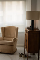 Beige armchair next to a wooden side table with a lamp in a room with striped wallpaper.