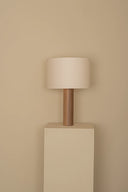 Floor lamp with wooden base and beige shade against a beige wall