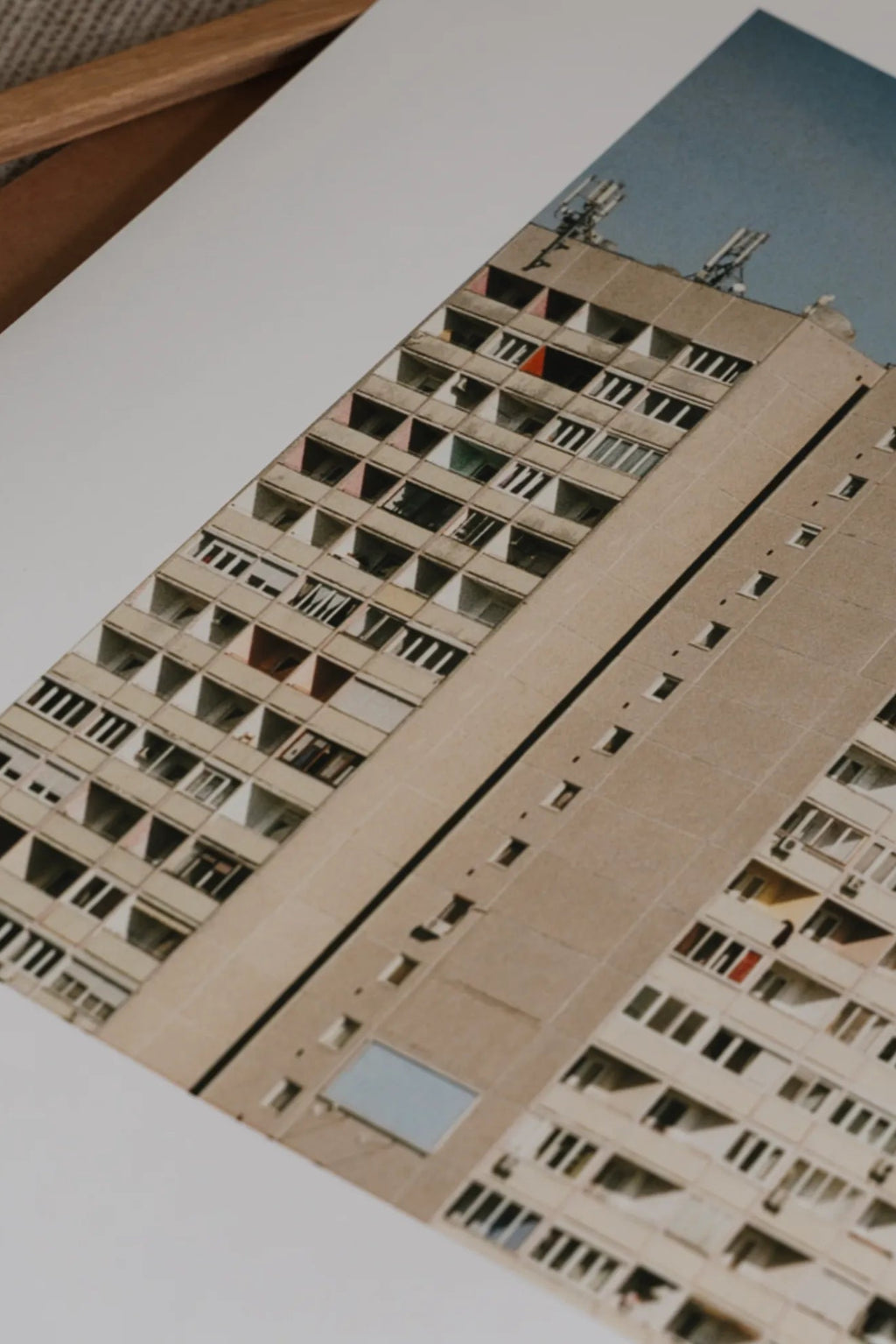The Poster Club Block O’Clock, a striking brutalist architectural photography print featuring a towering concrete apartment building under a muted blue sky, captured in an angled perspective with repetitive geometric windows and small pops of.