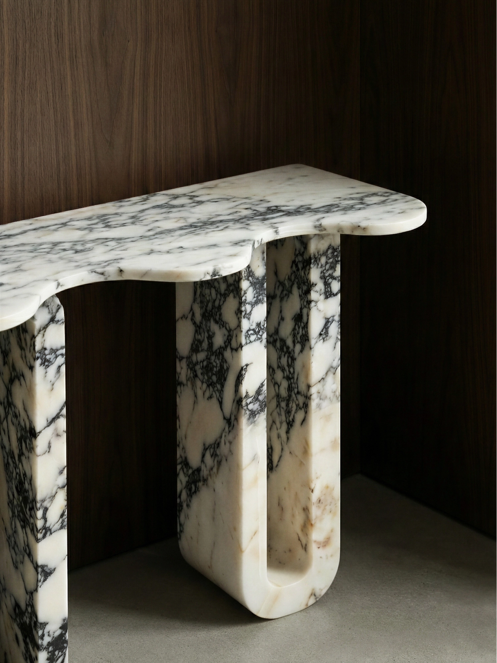 TCL Studios Pylon Marble Console, a sculptural white marble console table featuring dramatic black veining and a polished finish. Its organic curved tabletop rests on unique U-shaped legs with rounded edges, showcasing natural warm undertones within the cut-out. Ideal as a luxury statement piece for modern minimalist entryways or contemporary living rooms.