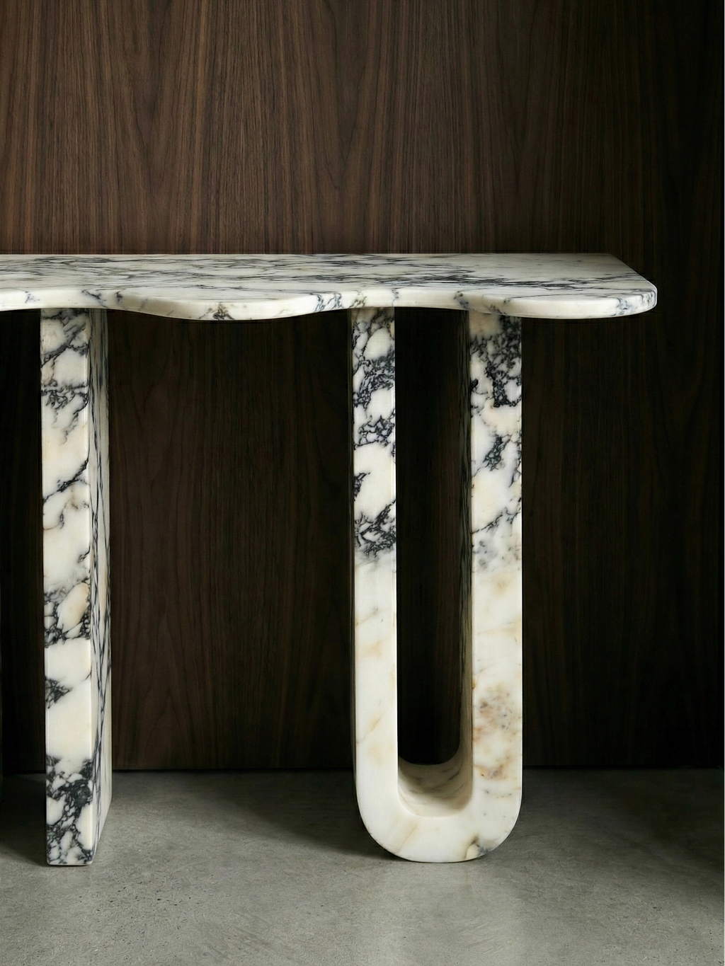TCL Studios Pylon Marble Console, a luxurious modern console table crafted from exquisite white marble with dramatic dark grey and black veining, featuring a distinctive wavy tabletop edge and bold sculptural U-shaped legs. This contemporary natural stone entryway table embodies an organic modern aesthetic, making it a striking statement piece for luxury living rooms, elegant hallways, or sophisticated minimalist interiors.