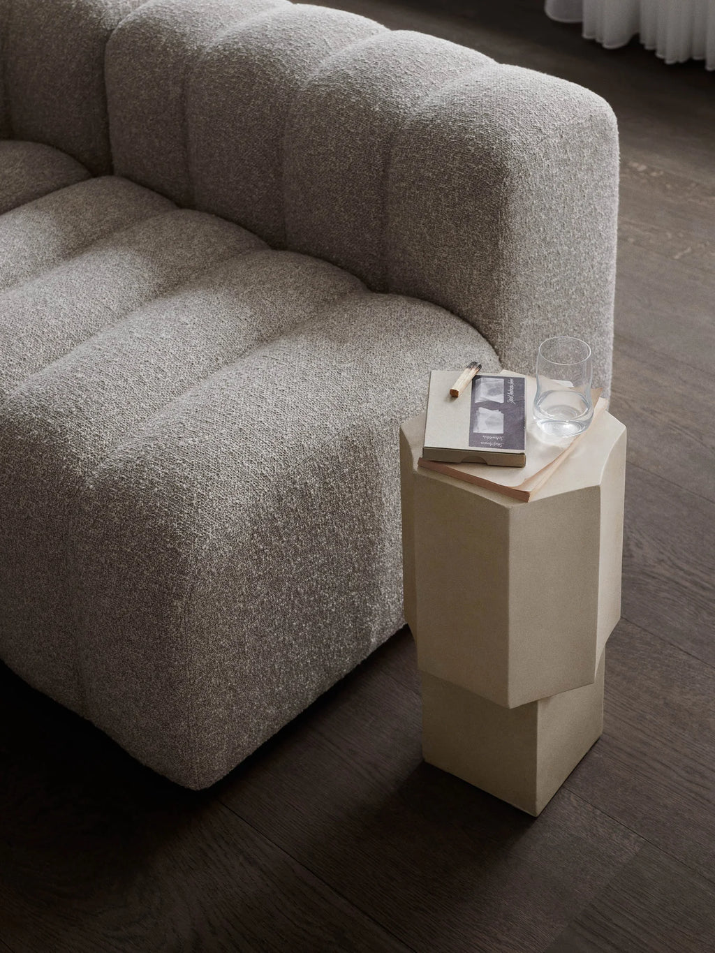 NORR11 Quartz Side Table, a modern and elegant hexagonal side table in a light taupe hue. This stylish piece features a unique geometric form, crafted from durable quartz, and rests on dark wood flooring next to a plush textured sofa. Perfect for adding a sophisticated touch to a living room or bedroom for design-conscious individuals seeking luxury home decor.