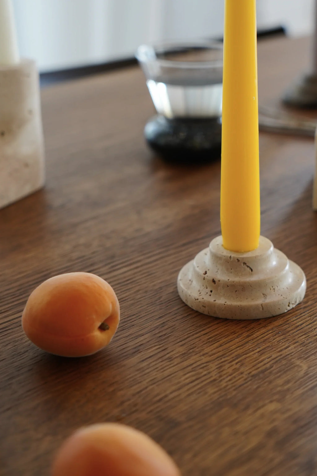 TAMO Rokk Candle Holder, a round, tiered, natural beige premium travertine candle holder with visible textured pores, holding a bright yellow taper candle. Perfect for elegant home decor.