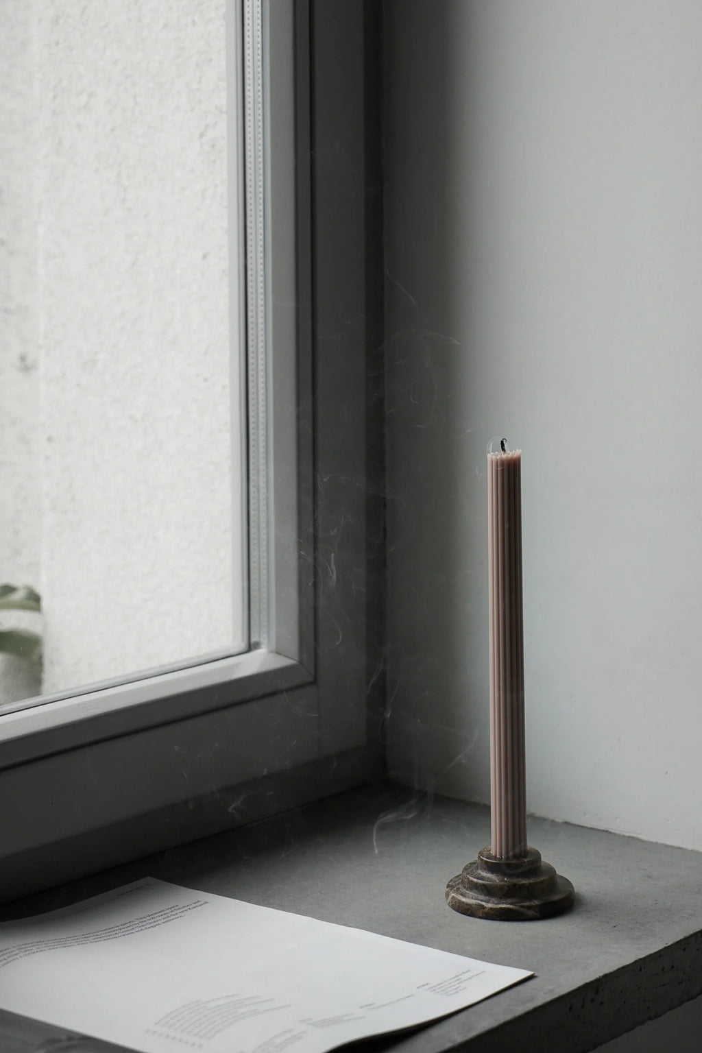 TAMO Rokk Candle Holder, an organic modern dark brown marble candle holder featuring a tiered, round base with natural veining, paired with a pale taupe fluted pillar candle.