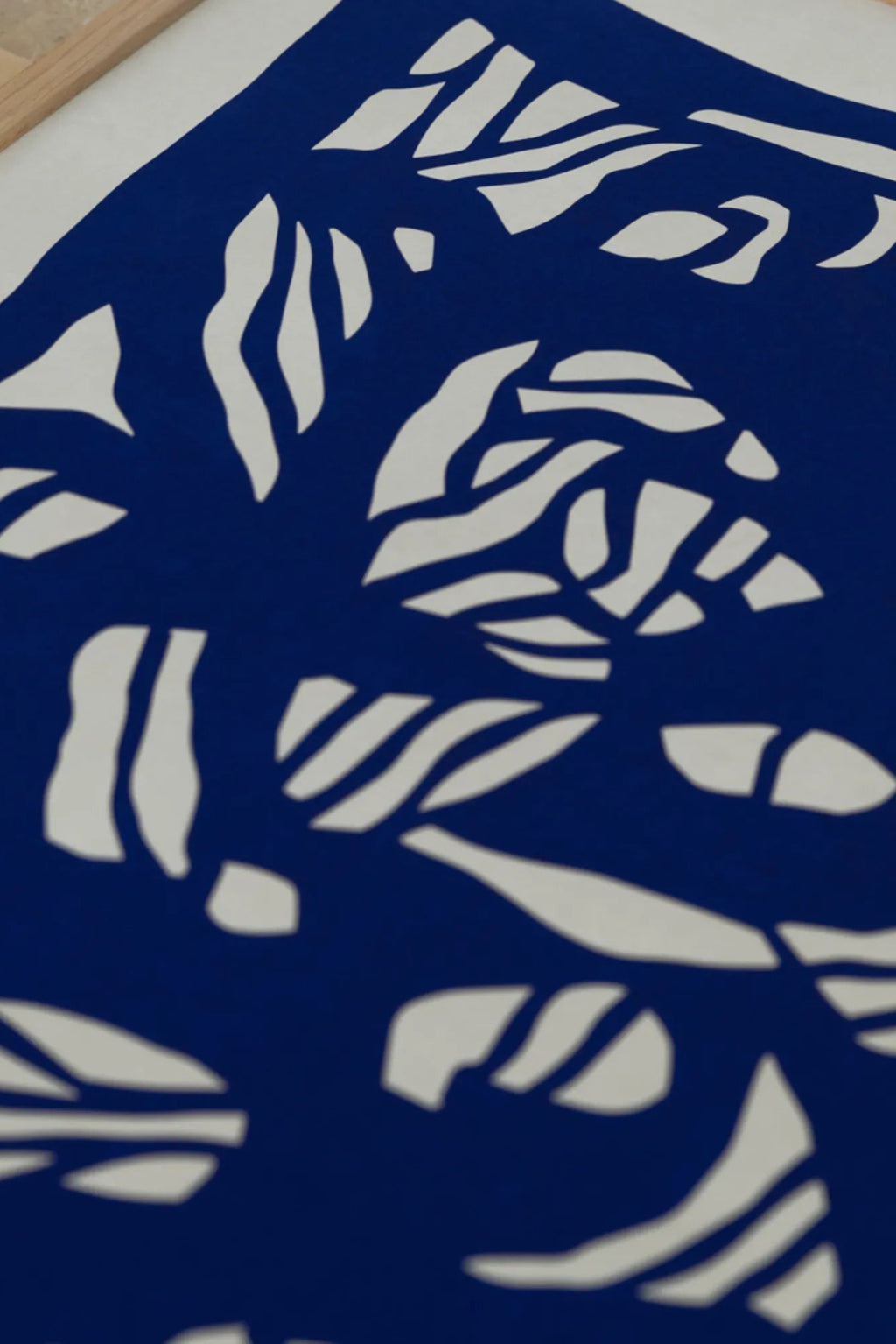 The Poster Club Root no. 03, a modern abstract art print featuring bold white organic botanical shapes in a striking cut-out style against a vibrant royal blue background, framed in a light natural oak frame. This minimalist botanical poster is perfect for contemporary gallery walls and Scandinavian-inspired living rooms or bedrooms.