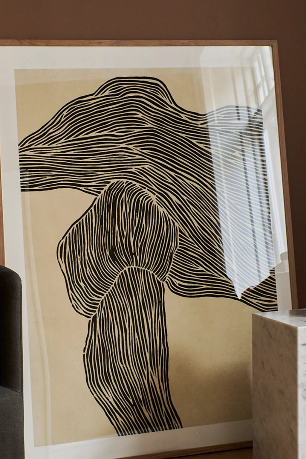 The Poster Club The Line No 16, a minimalist abstract art print featuring bold black organic lines that create a flowing, natural form against a warm beige background, presented in a sleek light natural oak frame. This contemporary graphic art print is perfect for adding refined visual interest to Scandinavian living rooms, japandi bedrooms, or organic modern gallery walls.