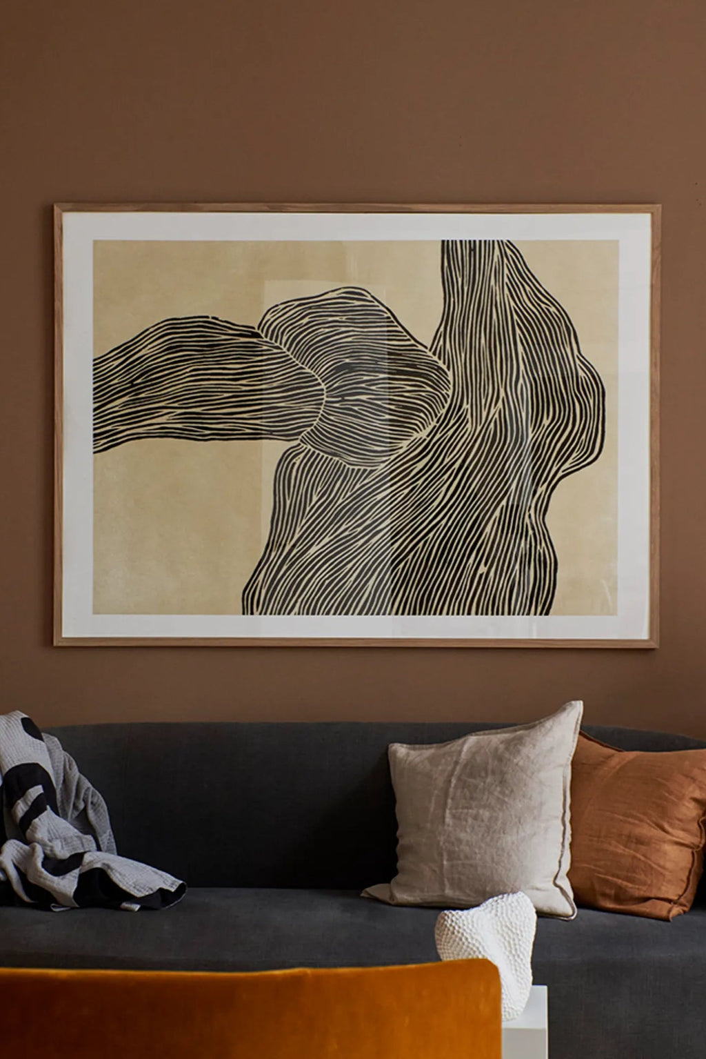 The Poster Club The Line No 16, a large abstract art print featuring flowing black lines forming organic, wavy shapes against a warm beige background. It is elegantly presented with a crisp white mat and a natural oak wood frame, offering a minimalist yet sophisticated aesthetic. This contemporary black and beige wall art is perfect for enhancing modern living rooms, Scandinavian interiors, or creating a striking gallery wall.