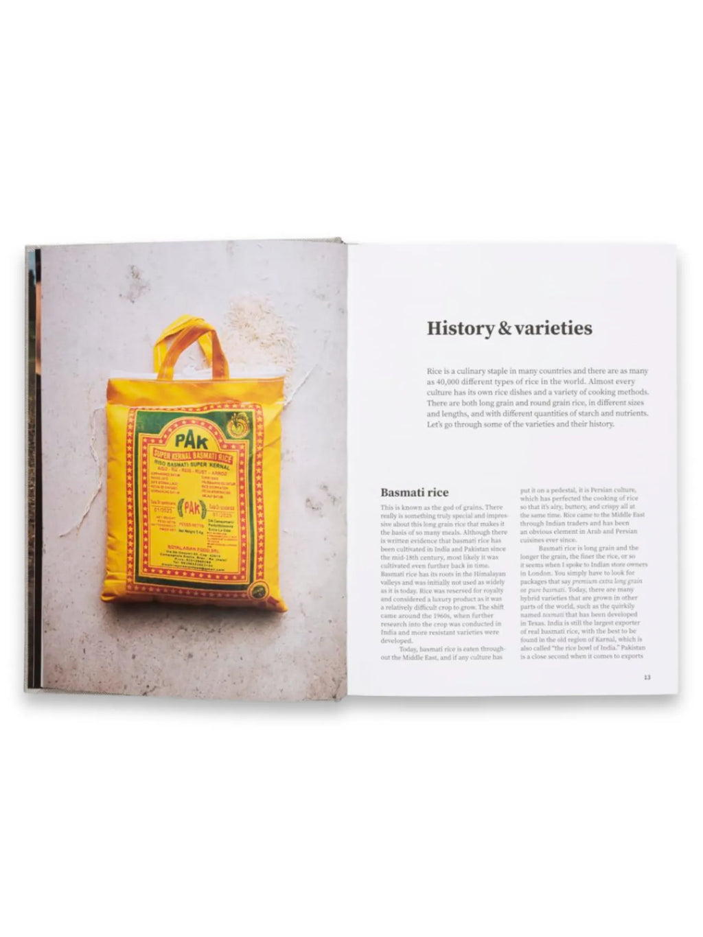 Book Rice and Shine, an open cookbook displaying a vibrant yellow "PAK Super Kernal Basmati Rice" bag on a textured gray background, beside a page with "History & Varieties" and "Basmati rice" text. This culinary book is perfect for food enthusiasts seeking detailed information and recipes about various rice types.