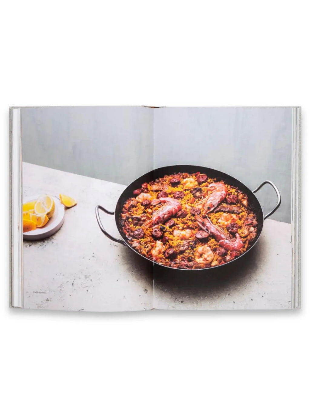 Book Rice and Shine, an open cookbook displaying a vibrant, detailed image of a paella pan filled with golden rice, large prawns, and dark meats. This culinary book is perfect for home chefs and food enthusiasts seeking inspiring and authentic recipes.