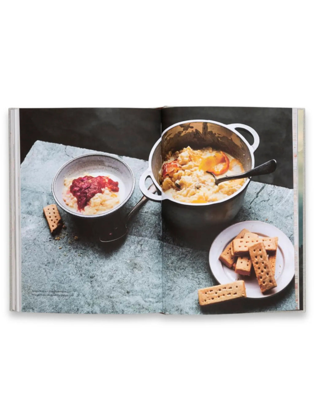 Book Rice and Shine, an open cookbook page displaying a delicious rice pudding recipe with vibrant red fruit topping in a small bowl, and a larger pot with creamy rice and fruit, accompanied by golden shortbread biscuits on a white plate, all resting on a textured gray surface. This culinary cookbook is perfect for home cooks seeking inspiring and comforting dessert recipes.