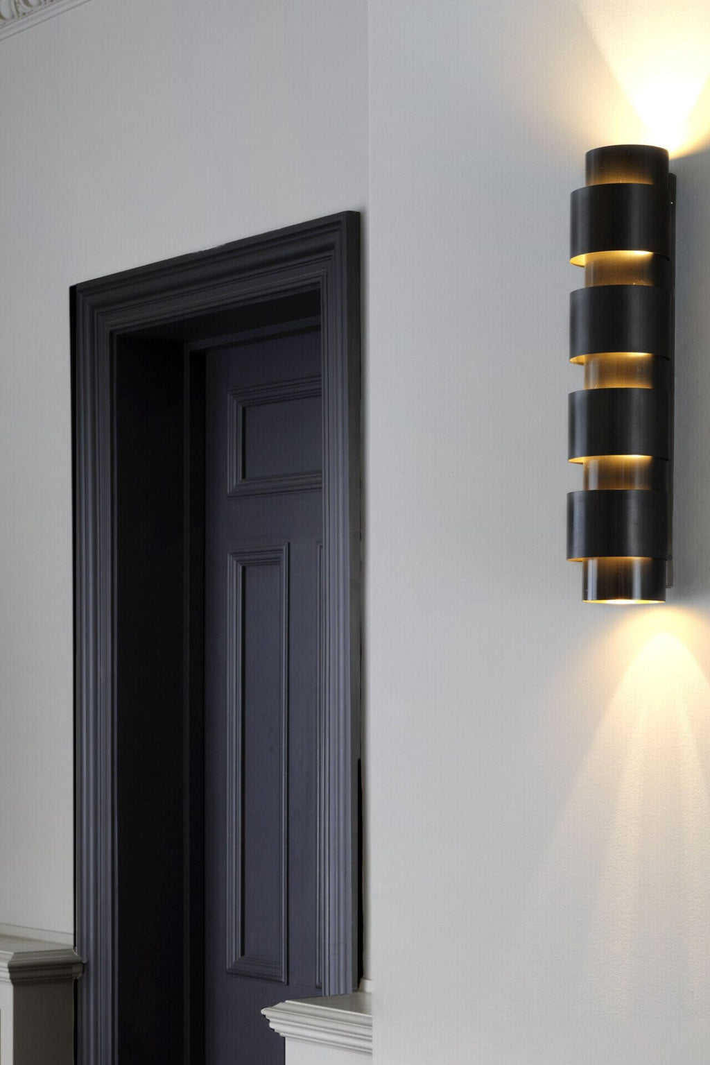 CTO Lighting Ring Tall Wall Lamp, a sophisticated modern wall sconce crafted from brushed dark bronze metal, featuring a distinctive stacked cylindrical ring design that emits a warm, inviting up-and-down.