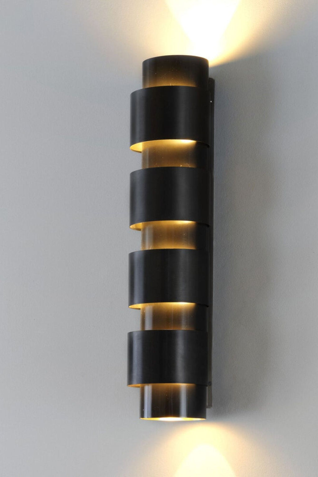 CTO Lighting Ring Tall Wall Lamp, a striking modern wall sconce crafted from dark bronze metal with a unique stacked ring design that casts warm uplight and downlight. This contemporary wall light features multiple open cylindrical bands, creating a sophisticated lighting effect for architectural interiors. Ideal for luxury living rooms, elegant hallways, or stylish bedroom accents.