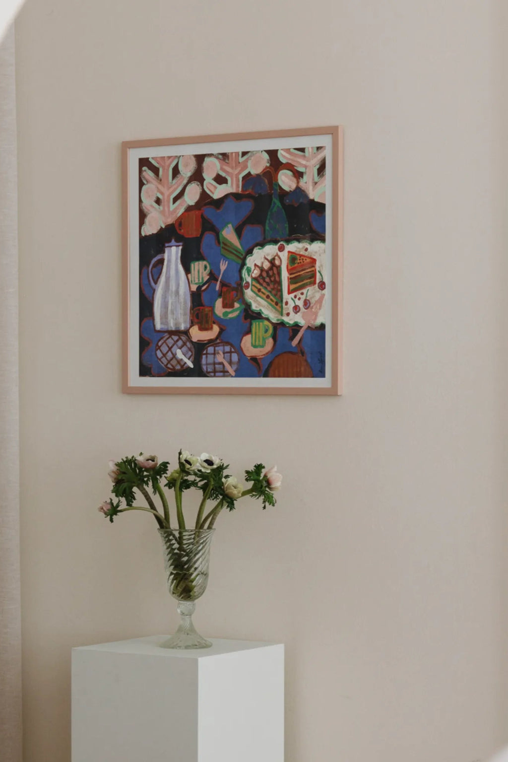 The Poster Club Cake, a vibrant abstract art print featuring an illustrative still life scene with two slices of cake, cherries, cups, and a pitcher set against a rich blue background with stylized pink and brown foliage. This contemporary poster, rich in deep blues, reds, greens, and creams, is framed in a light natural oak frame, adding a charming folk art touch to modern kitchen wall art, dining room decor, or a colorful gallery wall.