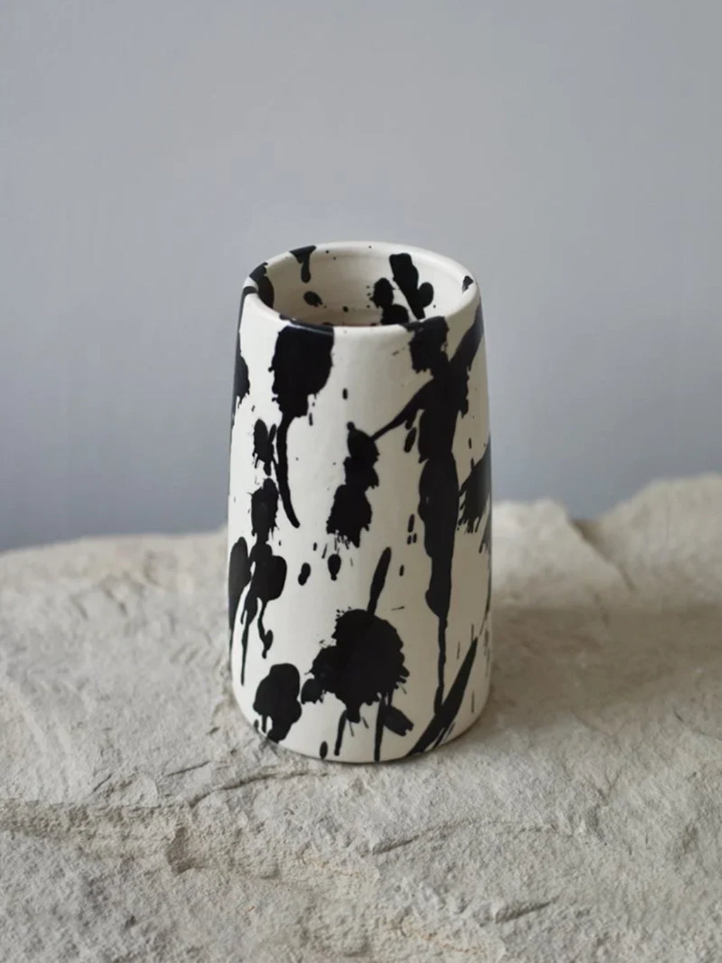 OWO Ceramics x That Cool Living Rock Vase II, a stylish handcrafted ceramic vase with a unique black ink splash design on a white matte finish. This elegant piece adds a modern, artistic touch to any home decor. Perfect for displaying single stems or as a standalone decorative accent for art lovers and minimalist enthusiasts.