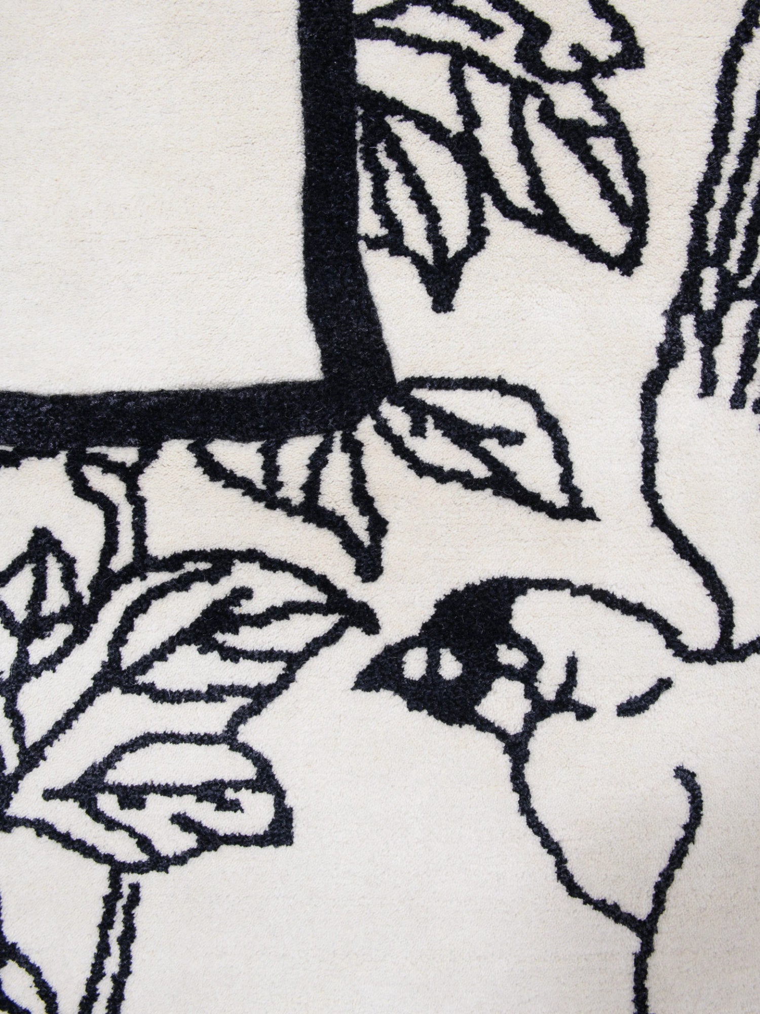 Haus Üger Shape of a Break Rug, a modern abstract rug featuring a plush cream-colored pile with bold, graphic matte black organic floral and leaf patterns.