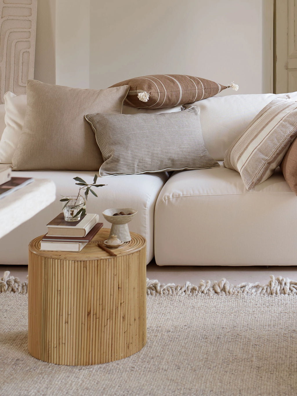 Tine K Viva Rattan Stool, a cylindrical organic modern side table crafted from natural light brown rattan with a distinctive vertical slatted texture. Its drum shape and warm tones make it a versatile accent piece, offering both style and functionality. Ideal as a boho bedside table, a coastal living room stool, or a minimalist accent table in various interior settings.