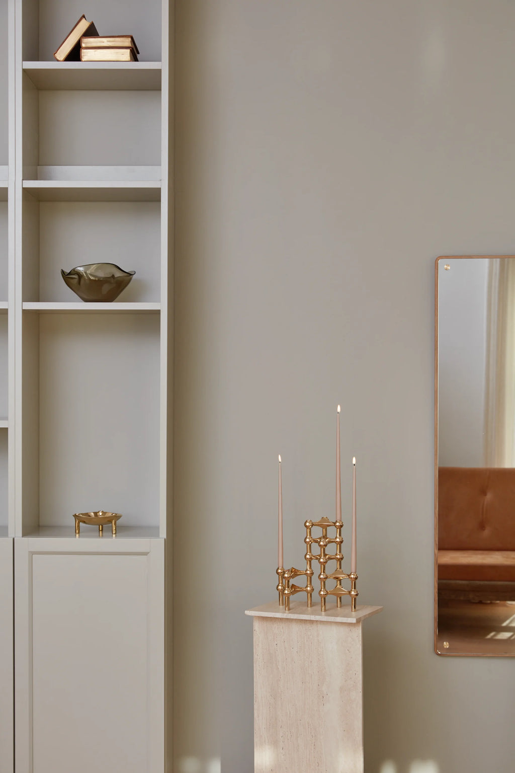 Stoff Nagel Candle Holder in a luxurious polished brass finish, holding three lit blush-pink taper candles, elegantly displayed on a light travertine pedestal in a contemporary living space.