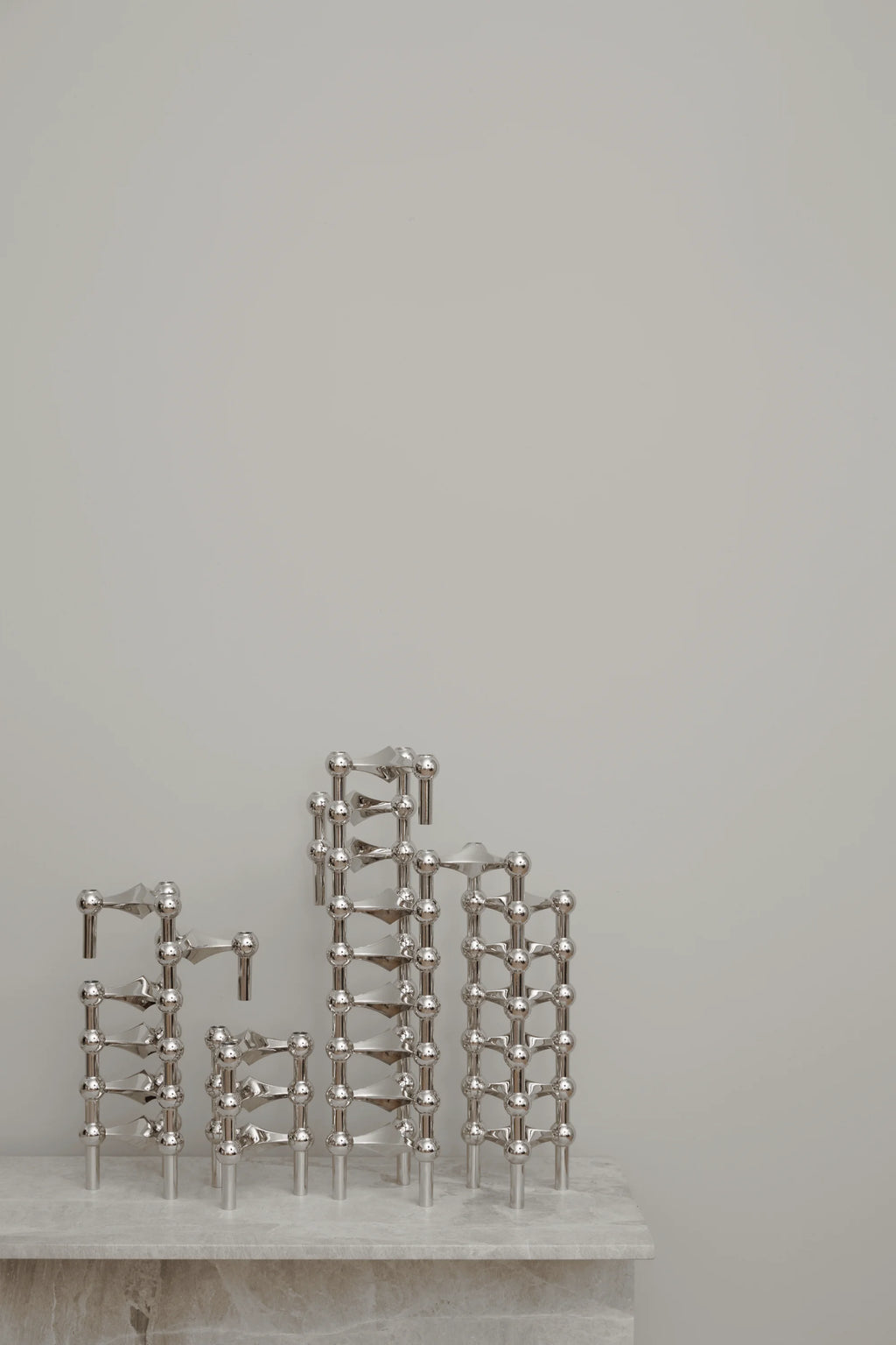 Stoff Nagel Candle Holder in a brilliant chrome finish, showcasing several modular units interconnected to form a dynamic, multi-level sculptural arrangement on a light gray marble surface.