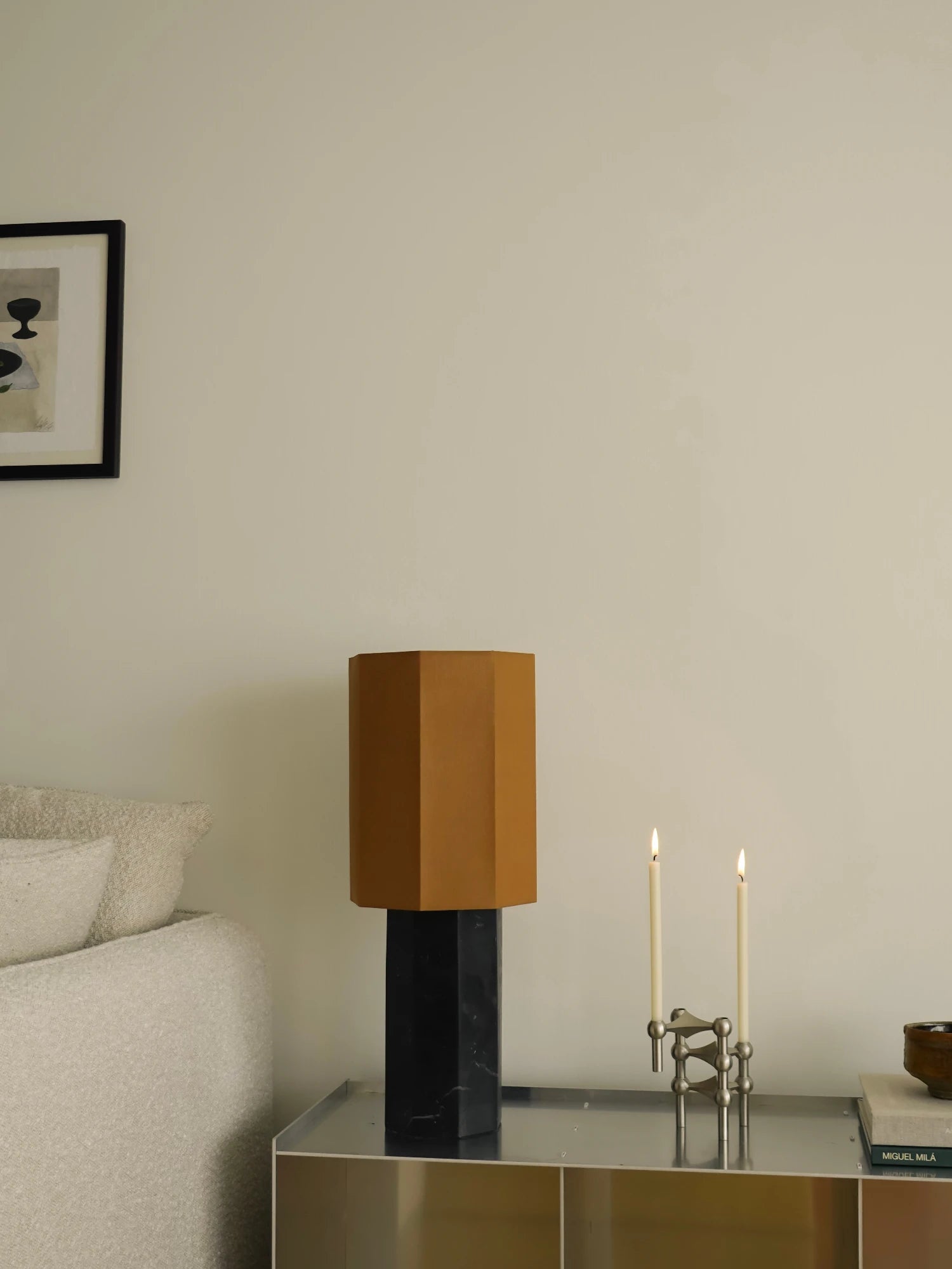 Modern interior with a geometric lamp on a table, taper candles and candle holder by stoff nagel, and a framed art print.