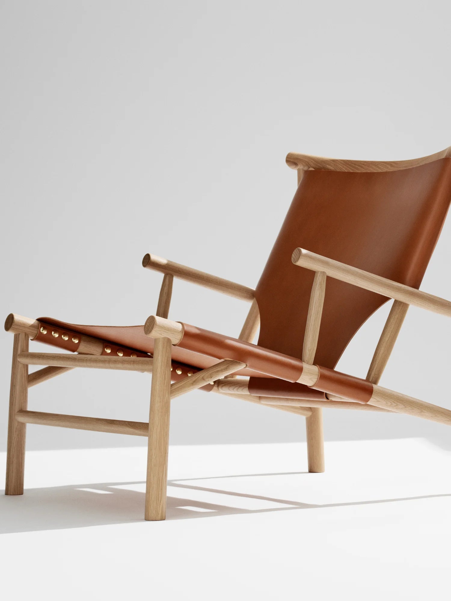 NORR11 Samurai Chair, a premium lounge chair featuring a modern design with natural oak wood frame and rich, tan leather upholstery secured by elegant brass studs. This stylish and durable chair provides a comfortable and sophisticated seating option for any contemporary living space.