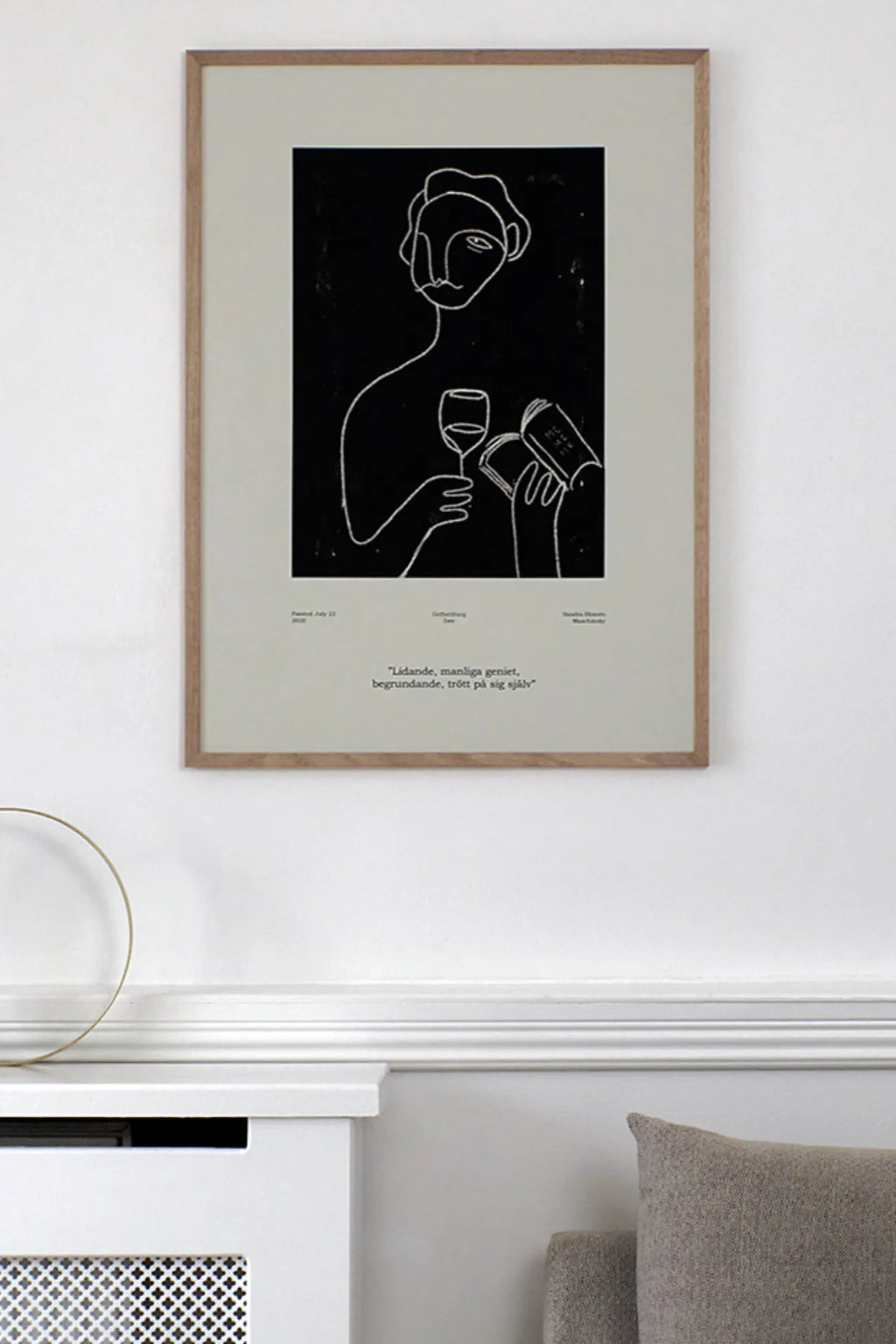 The Poster Club Genius, a modern minimalist abstract line art print featuring a person holding a wine glass and book rendered in expressive white lines on a solid black background, framed with a light natural oak frame and a wide cream mat. This contemporary black and white framed art is ideal for Scandinavian living rooms, a sophisticated home office, or a stylish gallery wall.
