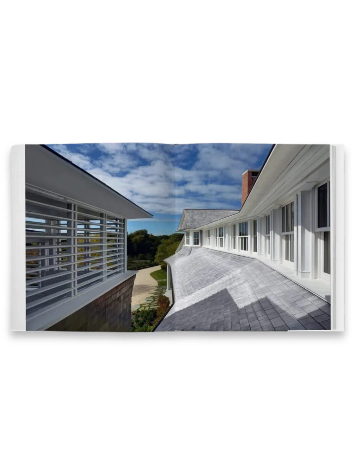 Book Shingle and Stone, showcasing an open book spread featuring a modern architectural residence with a light gray shingle roof and white slatted windows against a blue sky. This architecture book is perfect for design enthusiasts, architects, and homeowners seeking inspiration for contemporary coastal homes.