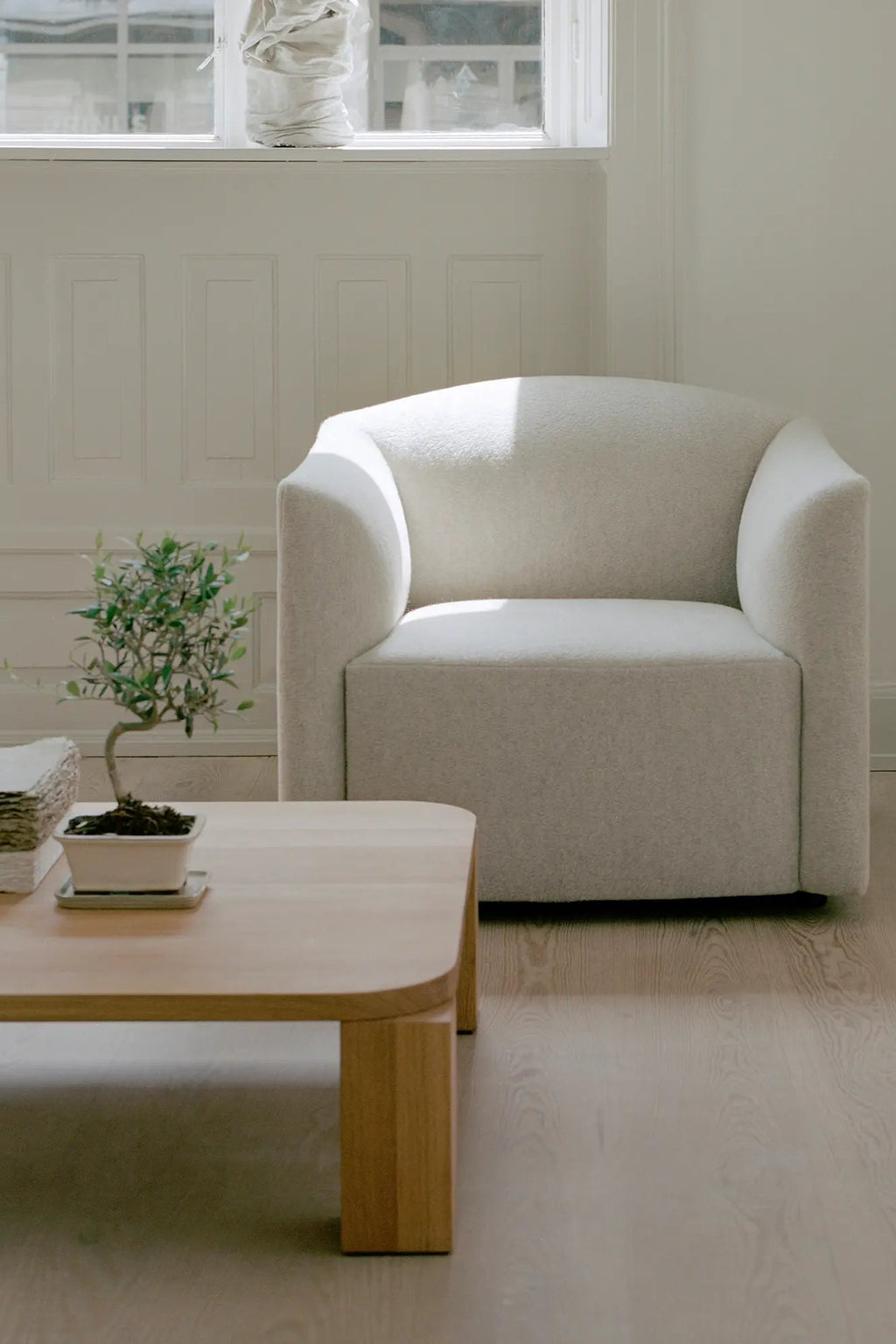New Works Shore Lounge Chair - Extended Base, a modern minimalist lounge chair upholstered in light grey textured bouclé fabric with a soft, sculptural curved silhouette and a low-profile extended base. This contemporary accent chair offers plush seating, perfect for living rooms, reading nooks, or Scandinavian-inspired spaces.