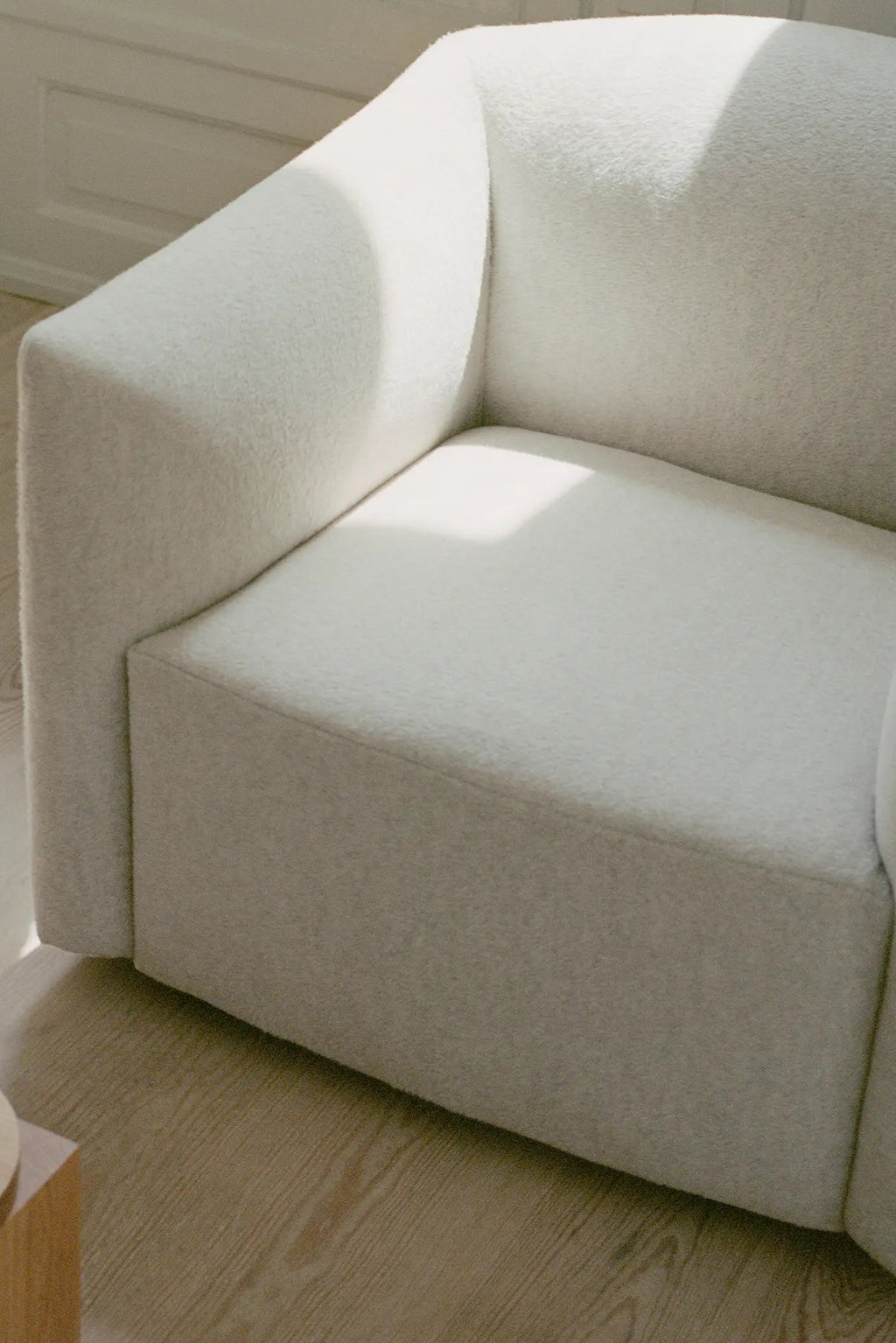 New Works Shore Lounge Chair - Extended Base, a contemporary organic modern lounge chair upholstered in a plush, textured cream bouclé fabric with soft, rounded arms and a low-profile silhouette. This minimalist armchair offers deep, comfortable seating, perfect for a modern living room or cozy Scandinavian-inspired reading nook.
