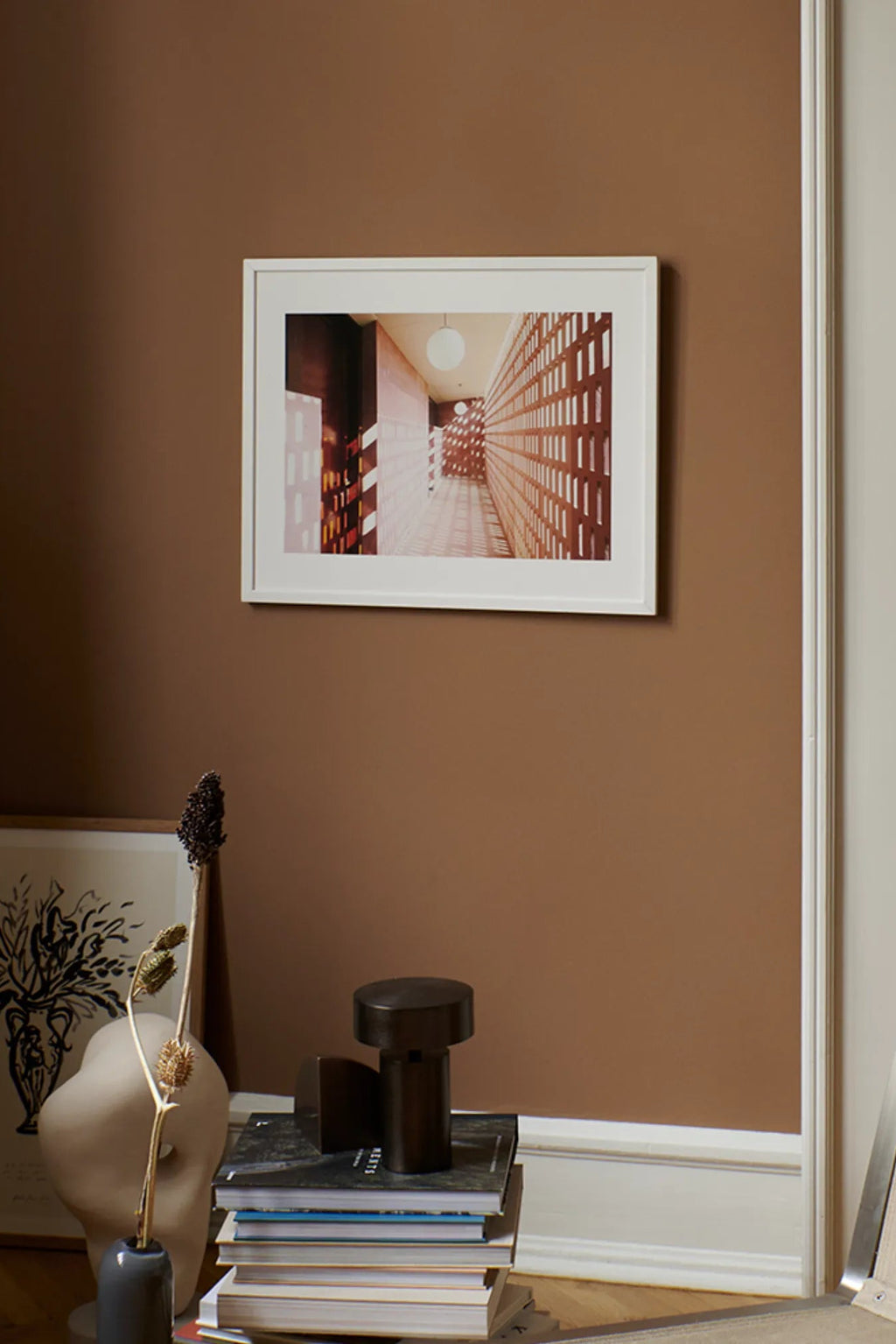 The Poster Club Lights, a modern architectural photography print capturing a long, minimalist corridor with warm terracotta-toned perforated brick walls and soft white globe lights, creating a striking play of light and shadow. This contemporary wall art, presented in a crisp white frame, is perfect for adding a sophisticated touch to modern living rooms, home offices, or gallery walls.