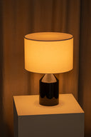 Table lamp with a warm glow on a wooden surface against a brown curtain background
