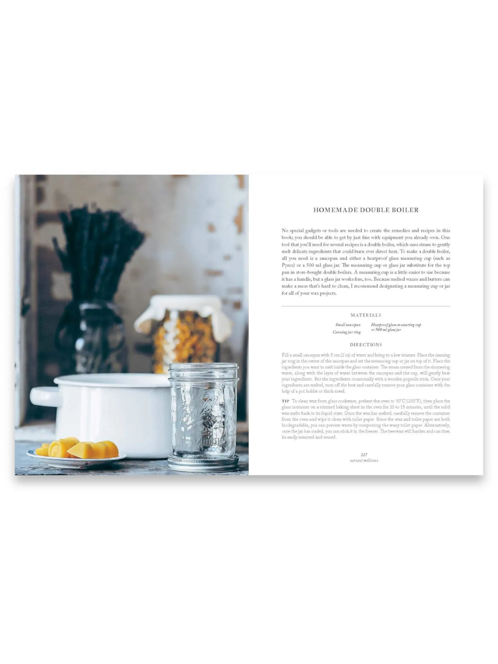 Book Simply Living Well, an open natural wellness book displaying text on a white page titled "HOMEMADE DOUBLE BOILER" next to a vibrant photograph showing a white enamel pot, a clear glass canning jar with a silver lid, and yellow beeswax chunks on a small plate. This helpful guide provides practical DIY recipes and home remedies for readers interested in sustainable living and natural wellness.
