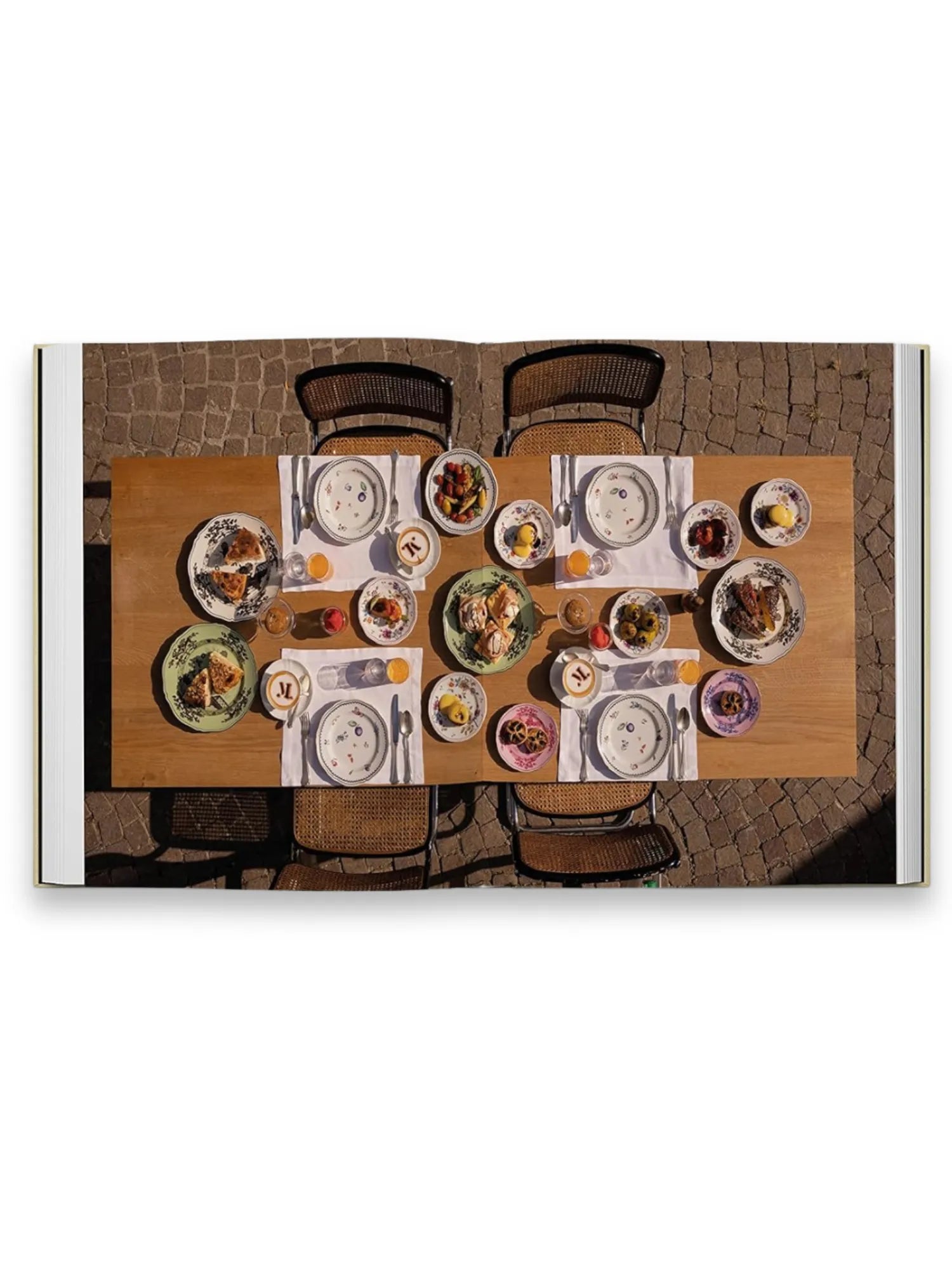 Book Slow Food, Fast Cars, featuring an aerial view of a rustic outdoor dining table set for several guests, adorned with colorful ceramic plates filled with various dishes, clear glasses of orange juice, and white napkins. This engaging lifestyle book is perfect for culinary enthusiasts and travel lovers seeking inspiration for vibrant dining experiences.