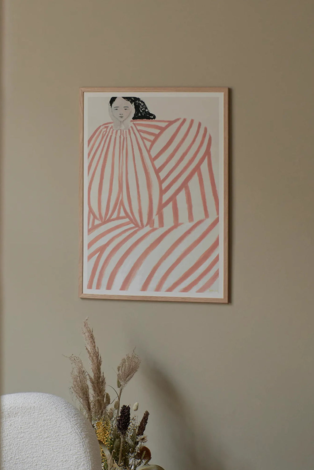 The Poster Club Still Waiting, a contemporary abstract art print depicting a seated figure rendered in bold, hand-painted coral and white stripes that create a sense of flowing movement. This graphic art piece features a minimalist palette with subtle brushstroke textures, framed elegantly in a light natural oak frame with a crisp white mat.