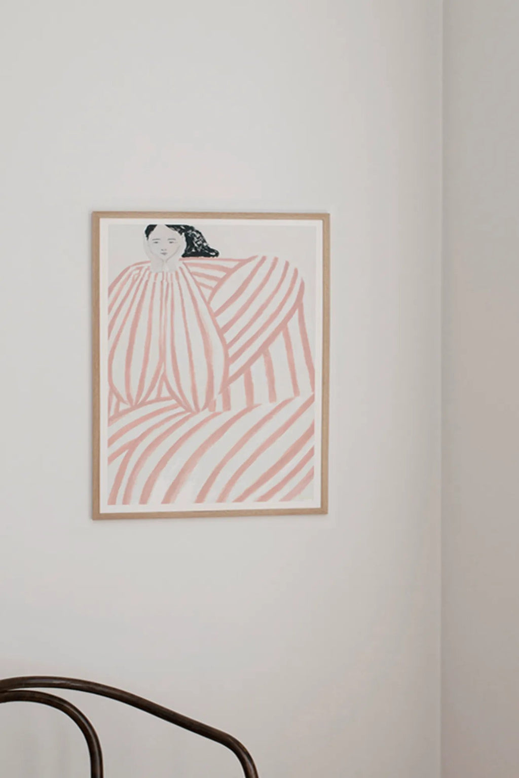 The Poster Club Still Waiting, a minimalist abstract art print depicting a pensive abstract figure with black hair against a cream background, characterized by soft blush pink and white stripes in varying directions. This contemporary framed poster, presented in a light natural oak frame with a clean white mat, is perfect for adding organic modern wall art to Scandinavian bedrooms or gallery walls.