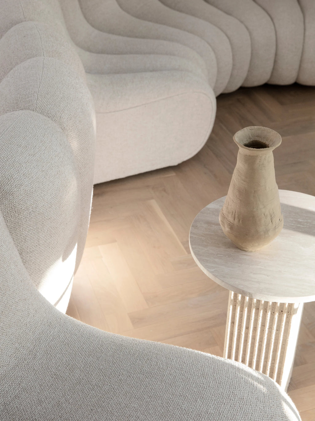 NORR11 Soho Side Table, a round travertine side table featuring a smooth polished natural stone top and a distinctive fluted cylindrical base, showcasing beautiful light beige and cream tones. This organic modern accent table is perfect for minimalist living rooms, contemporary bedrooms, or as a stylish natural stone end table.