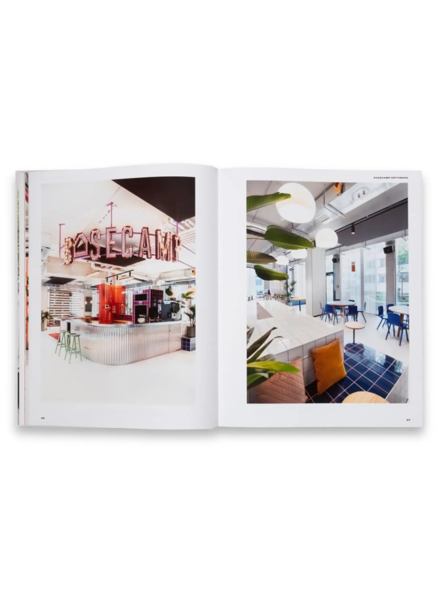 Book Spatial Storytelling, an open book displaying vibrant interior design photographs. The left page features a modern cafe with a corrugated metal counter and pink neon "BASECAMP" sign, while the right page shows a contemporary lounge area with blue tiled flooring and white pendant lights. This inspiring design book is ideal for architects, interior designers, and decor enthusiasts seeking creative spatial concepts.