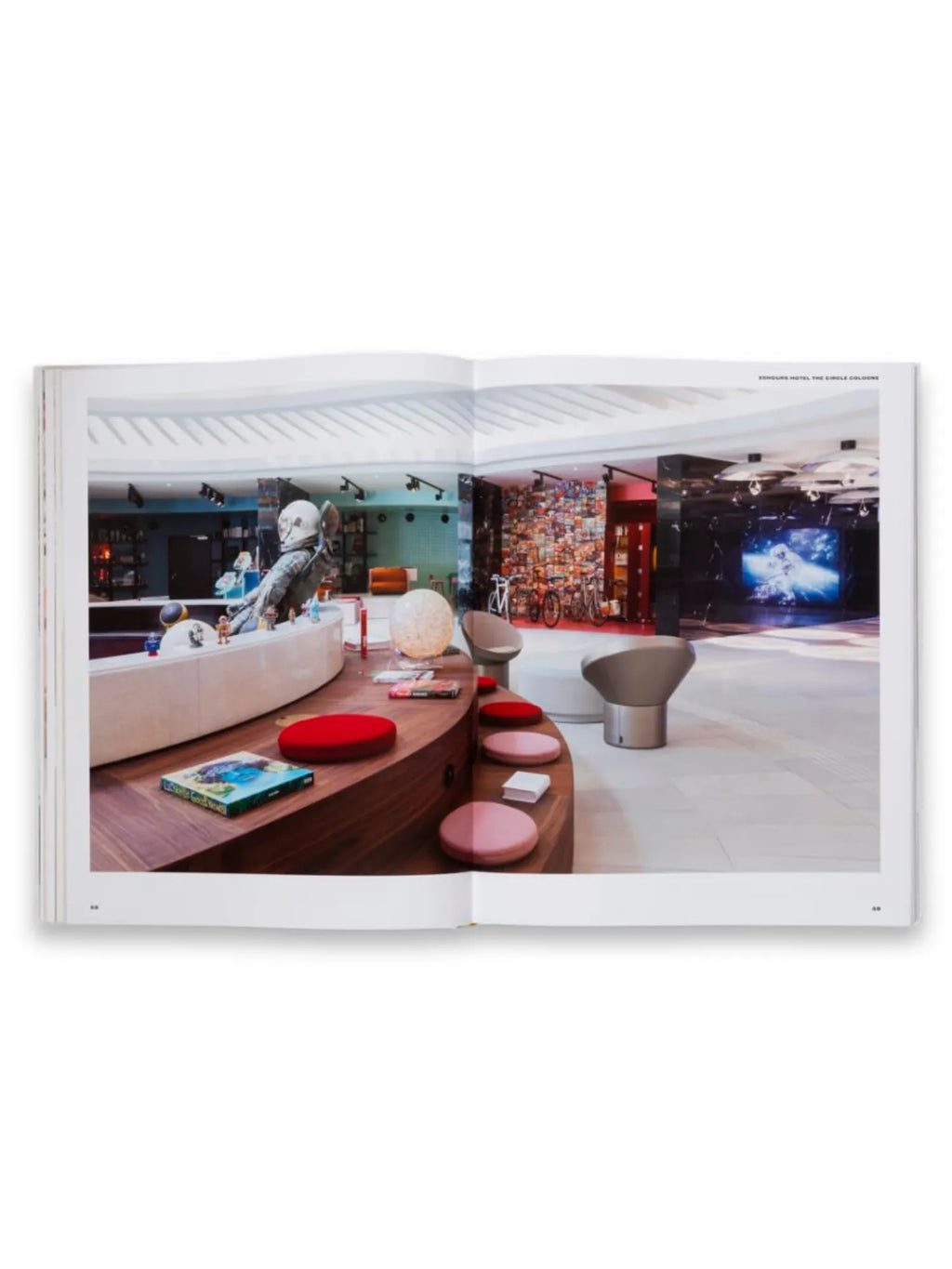 Book Spatial Storytelling, an open book displaying a vibrant, modern hotel lobby with a curved wooden counter, red and pink cushions, and an astronaut sculpture. This engaging design book is perfect for interior designers, architects, and art enthusiasts seeking inspiration for innovative spatial concepts.