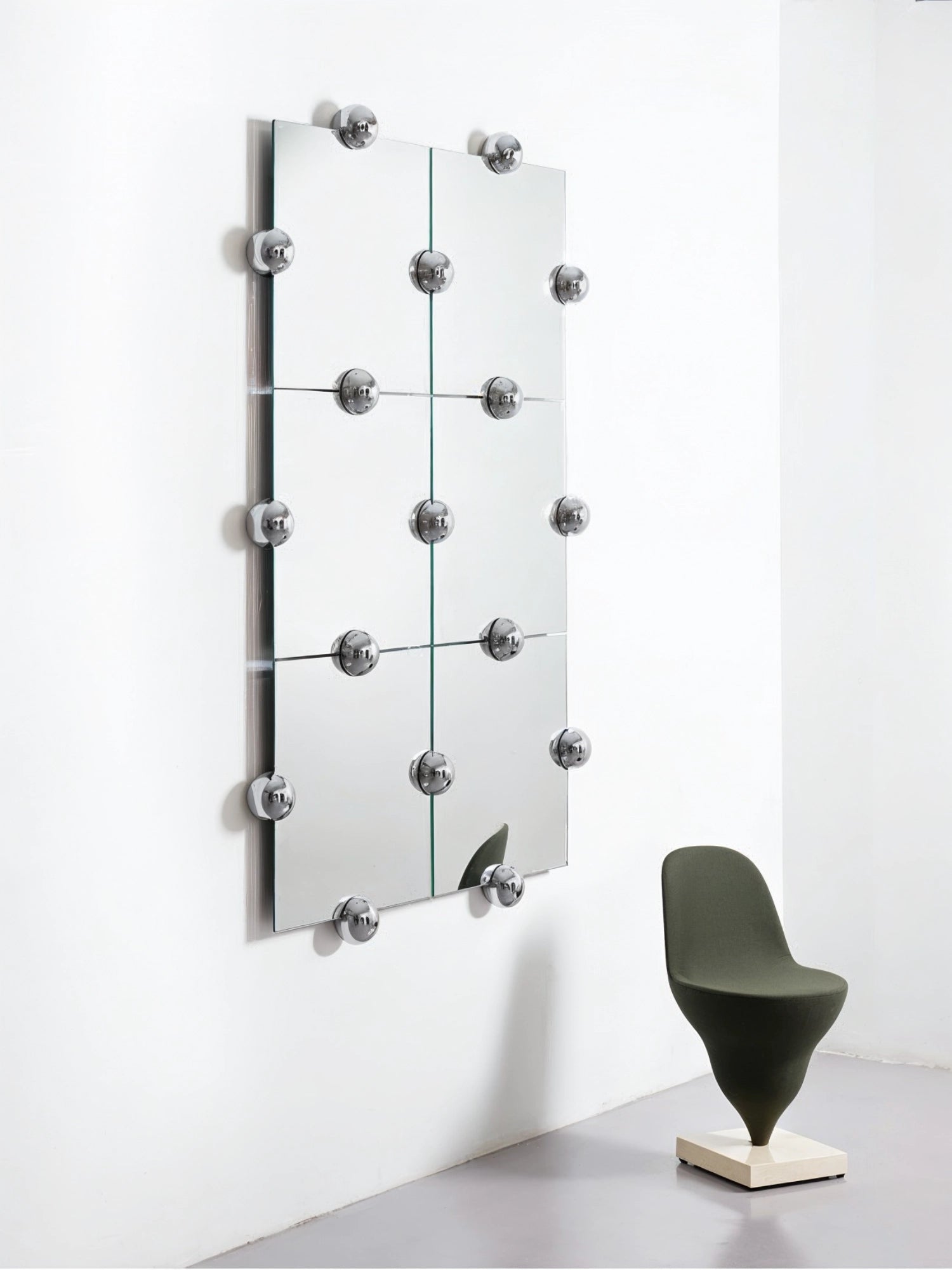 Moustache Sphera Crystal Palace L Vertical Mirror, a tall, modern modular mirror composed of six square panels, accented with numerous polished chrome spherical fasteners, next to a green chair.