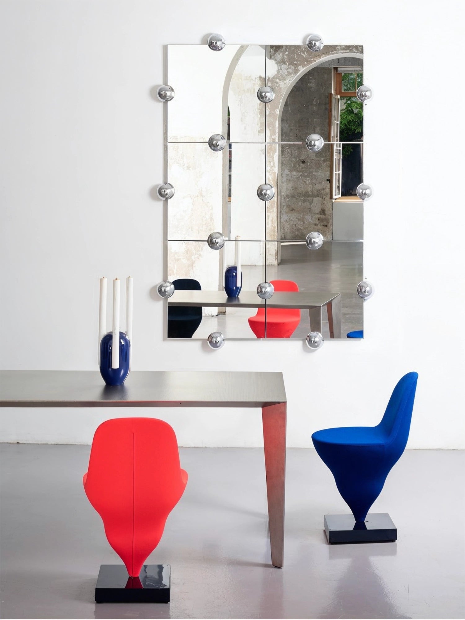 Moustache Sphera Crystal Palace L Vertical Mirror, a grand modular mirror with six square panels and chrome spherical fasteners, reflecting a stylish dining area with red and blue chairs.