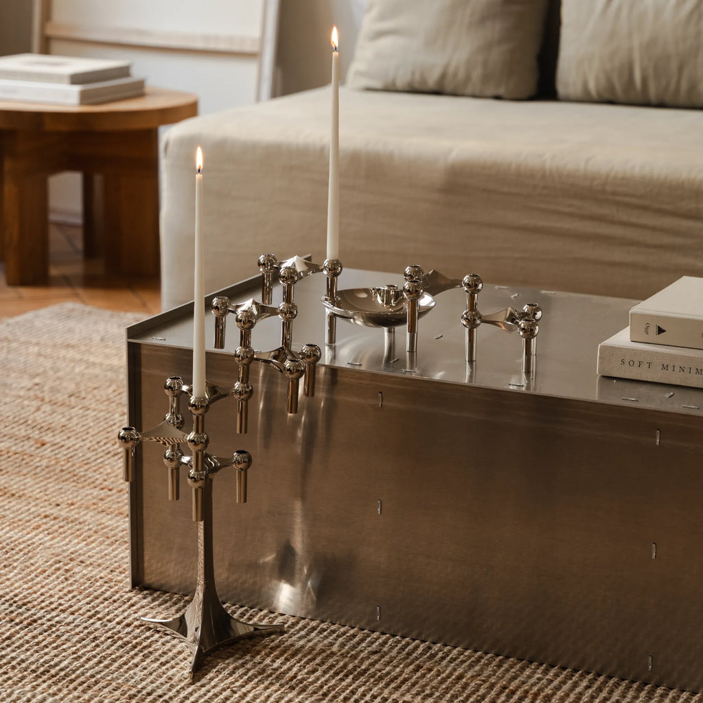 Stoff Nagel Candle Holder Stand, a modular mid-century modern design icon crafted from polished chrome-plated metal, featuring a geometric, sculptural form with spherical joints that can be stacked and arranged to create unique configurations. This reflective silver candle holder, shown with tall white taper candles, embodies minimalist Danish design. Perfect as a striking dining table centerpiece or for modern shelf styling in contemporary living rooms.