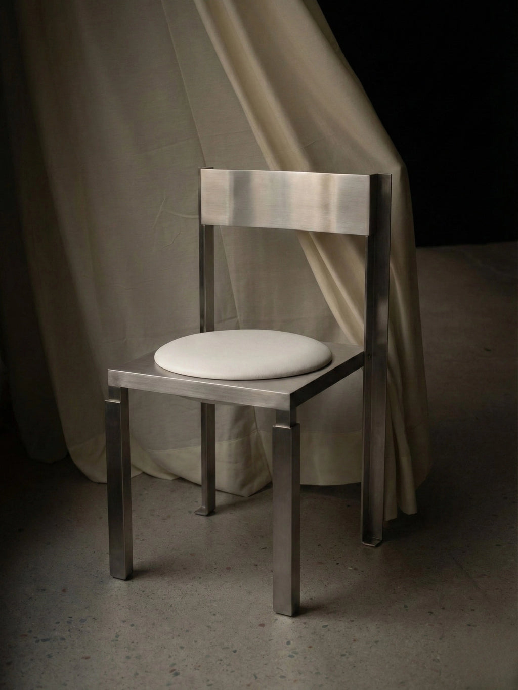 YET. Strut Chair, a sleek modern minimalist dining chair crafted from brushed stainless steel with a bold, rectilinear frame and a contrasting circular white upholstered seat. Its industrial chic design features clean geometric lines and a sturdy, architectural presence. Perfect as a contemporary dining chair or a brutalist accent piece for modern living spaces.