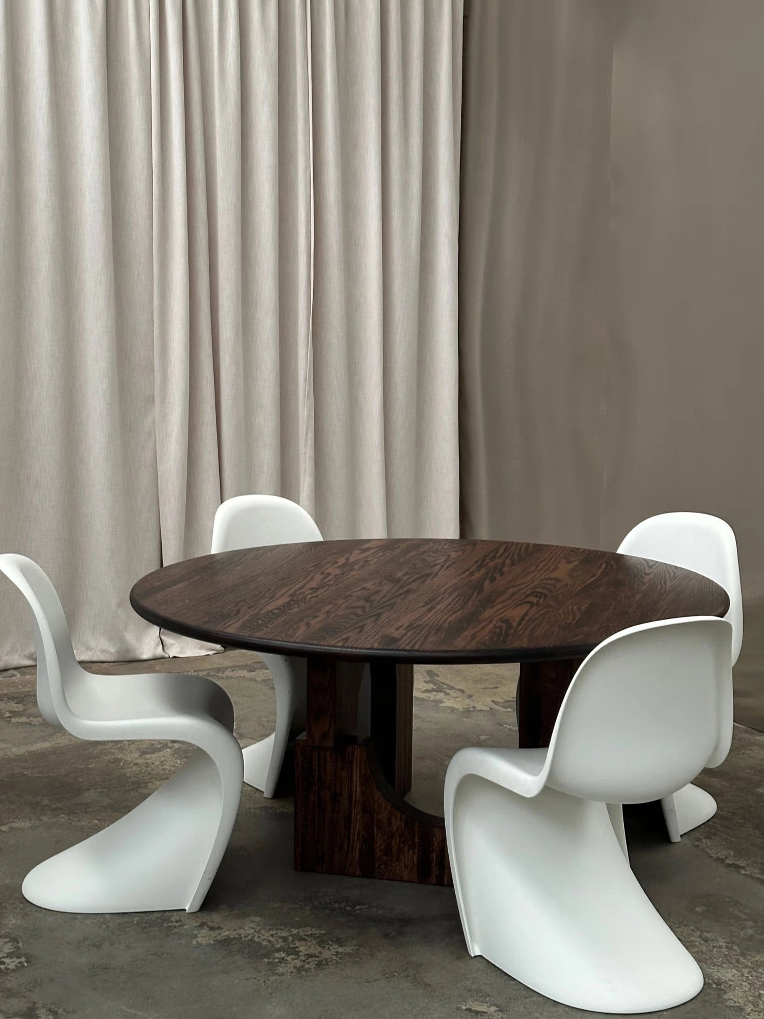 Tinted Objects Sanders Round Dining Table, featuring a rich, dark brown oak wood top with visible grain and a sturdy, sculptural pedestal base. This elegant dining table is perfect for modern homes seeking a sophisticated and durable centerpiece.