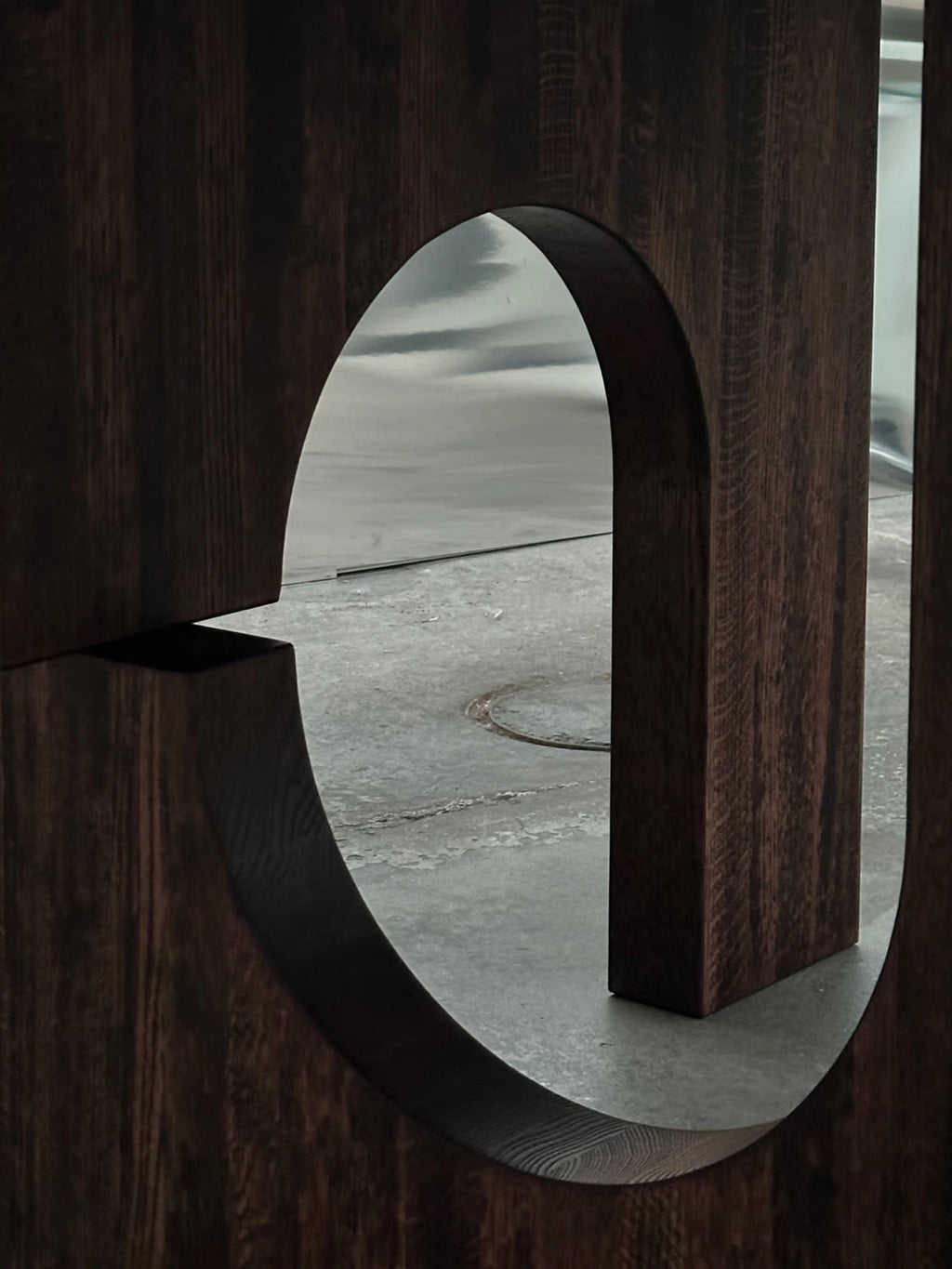 Tinted Objects Sanders Round Dining Table, showcasing a close-up of a rich dark brown wooden table base with prominent grain, featuring an elegant, large circular cutout design. This modern dining table is perfect for those seeking sophisticated, contemporary furniture for their home.