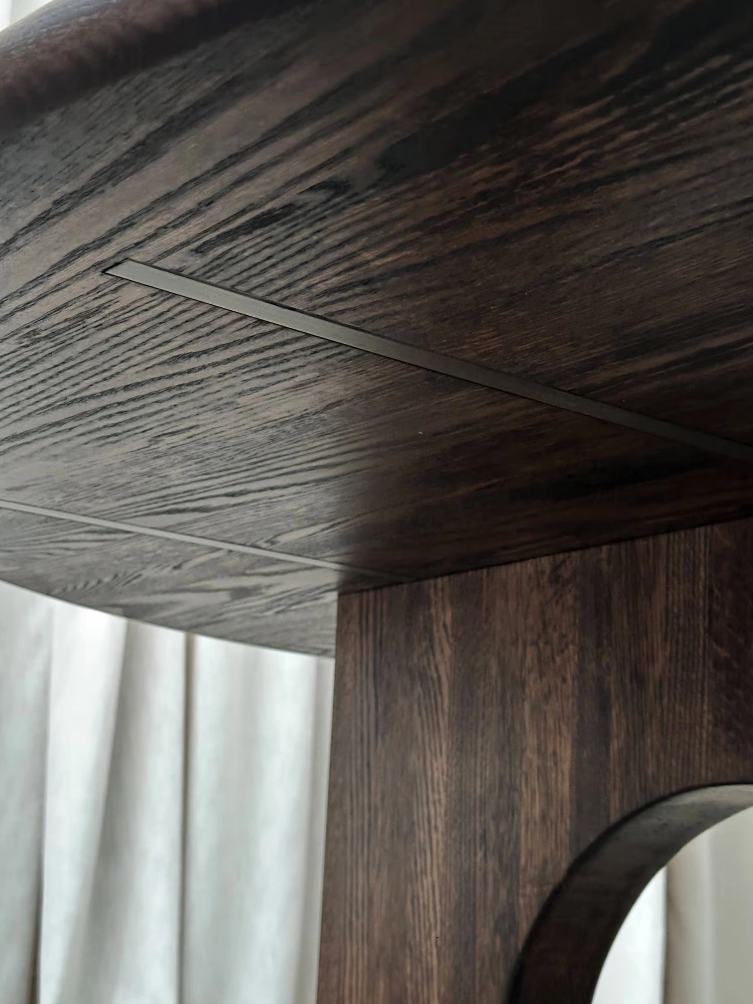 Tinted Objects Sanders Round Dining Table, featuring a rich, dark brown oak wood grain with subtle dark gray metallic inlays near the table's edge and along the pedestal base. This elegant, modern dining table is ideal for contemporary homes and design-conscious individuals seeking a stylish and durable centerpiece.